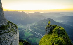 Hiker stands and enjoys valley view from hilly viewpoint. Traveling on hill peaks landscape. Sport, tourism and hiking concept. Watching sunset.