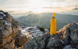 Yellow outdoor travel water bottle. Male hand holding bottle. Mountains and winter in national park in during sunset. Travel concept, drink water, adventure  