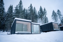 Modern wooden log cabin and snow covered trees in winter Finland Lapland. Secluded tiny house. Private house near forest. Country house. Trail goes to cottage in middle of snowdrifts.