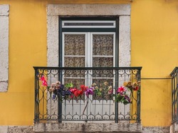 Traditional Portuguese house, with white plastic windows and ornate metal balcony railings. Part of old and yellow building wall.