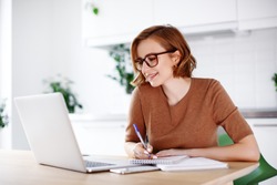 Woman on remote work or online education, using laptop computer, making  notes, indoors at office or home at daytime. Online business, young professional at workplace. Working from home.