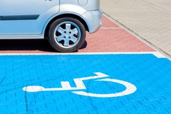 Blue car parking spot for the disabled, handicapped. Wheelchair symbol painted on the ground, parking lot vehicle space, closeup, angled view, nobody. Disability and city transportation concept