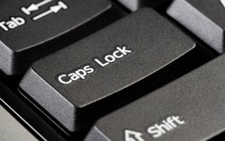 Single caps lock key on a simple black desktop PC computer keyboard, object detail, extreme closeup. Using capital letters, typing in all caps, screaming, shouting, emphasis abstract concept, nobody