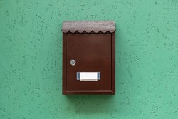 One single simple locked apartment letterbox with an empty blank name tag, classic traditional residence mailbox hanging on a green wall, metal mail letter box front view, object closeup, nobody