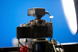 A modern professional high end mirrorless video camera on a tripod stand, bluescreen chroma key studio background, lights, live transmission recording, broadcast, media streaming concept, nobody