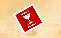 Red fragile cargo package sticker label on a wooden box crate container, detail, closeup, top view, from above, nobody. Cracked wine glass symbol. Logistics, fragility, delivery transportation concept