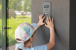 Elementary school age child, girl using a door entry phone, entering the entry code alone outdoors, block of flats, residential area building entrance doors. Paying a visit, visiting simple concept