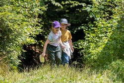 Two children, girls, curious kids exploring the forest together walking through green lush foliage alone, adventure and exploration simple concept, One with nature, forest walk, two people, lifestyle