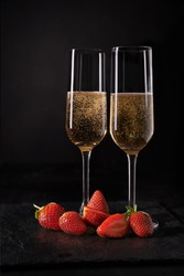 two glass with champagne and strawberries over dark background