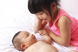 Little sister hugging her newborn sister. Toddler kid meeting new sibling. Cute girl and new born baby girl relax in a white bedroom. Family with children at home. Love, trust and tenderness.