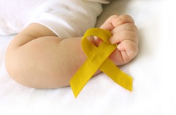 Childhood cancer awareness gold ribbon on human hand and baby background.Gold ribbon symbolic concept raising campaign support help childhood cancer awareness,