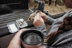 Coffe in a thermos cup with truck bed and a flybox in the background. Gearing up for flyfishing.