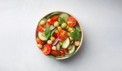 Vegetarian chickpea salad prepared with tomatoes, cucumber, red onion, cress salad and arugula in a paper bowl. Chickpeas are rich in protein and fiber. Zero waste dishware, top view