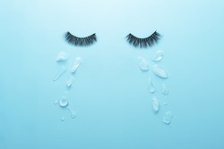 Creative concept of sadness. Glued lashes on a blue background with tears in the form of ice pieces.  