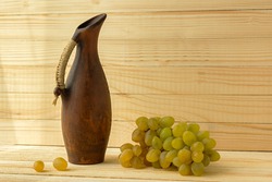 Grape jug on a wooden natural background. Rustic retro style. Antique clay jug with wine. Green juicy ripe grapes of the autumn harvest. the concept of agriculture, winemaking. Horizontal still life