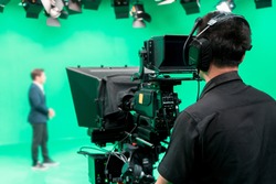 Cameraman working with announcer in broadcast television green screen studio room and professional camera.