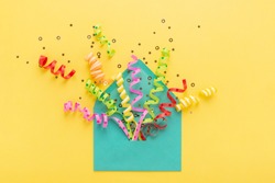 Envelope with party confetti explosion on yellow background. Invitation card, flat lay.