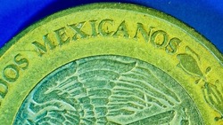 Microscopic view of engraved letters of Mexicanos on a old bimetallic ten pesos coin of Mexican dollar with grime, scratches, and dents