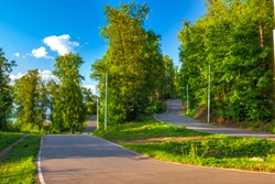 Asphalt road track turn in a sunny green forest among the colorful trees on a summer clear day with a blue sky. Biathlon Stadium, Ufa, Bashkortostan, Russia.
