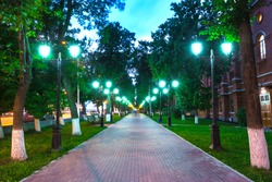 Pavement walkway at night in the green light of symmetrically lampposts, leading to the center of the frame. Pushkin street near the Opera and Ballet Theater, Ufa, Bashkortostan, Russia.