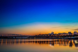 View of the night city from the river bank. Bridge leading to the city on a sunset background. Welcome to UFA, Russia.