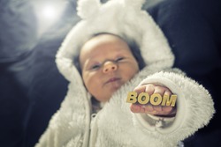 Newborn baby holding up a golden knuckle duster that reads the word BOOM.