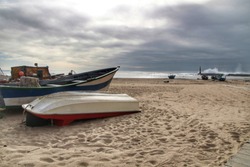Fishing boats stranded on Aguda beach and Giant waves breaking on the breakwater and the lighthouse on Aguda Beach