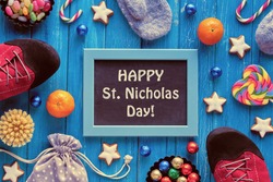 Text Happy St Nicolas Day on blackboard, chalk board. Traditional holiday in Germany and Western Europe on December 6. Various sweets, candy, cookies and rainbow heart. Flat lay on turquoise wood.