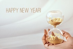 Hourglass, passage of time from 2021 to 2022 year. Wood artistic model hand holding time glass. Countdown to winter holidays. Merry Christmas and a Happy New Year.