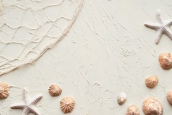 Summer beach background with brown seashells, starfish and pebbles. Fisherman net and shells on textured cream color background. Summertime monochromatic flat lay with natural decor,copy-space.