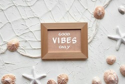 Text Good Vibes only in golden frame. Off white background with starfish, shells, seashells, necklace. Fisherman net on cream beige brown monochromatic background. Summertime motivation backdrop.