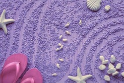 Summer by the sea. Magenta rubber flip-flops, slippers on pebbles with starfish, sea shells and pebbles, studio concept. Purple textured monochromatic background.