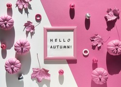 Pink fuchsia paper background with Autumn decor. Text Hello Autumn in frame. Monochromatic flat lay, magenta pumpkins. Hand with dry Fall leaves painted metallic pink.