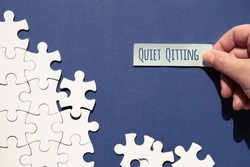 Quiet quitting text, caption. Jigsaw puzzle pieces half assembled and separate. Hand with sticky paper, office sticker. Top view, flat lay on monochromatic abstract blue white paper background.