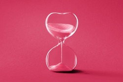 Hourglass, toned monochrome image in Viva Magenta color of the year 2023. Sandglass or sand timer. Single sand clock with golden sand on vibrant paper background. Design element,