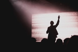 Solo artist raising hands at contemporary church conference silhouette against LED screen on stage
