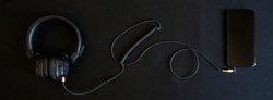 Black wired headphones with ear pads and a smartphone lie on a black background. Analog wire connection using mini-jack - 3.5 mm. Music and creativity. Banner