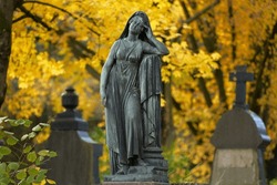 sad woman statue standing on a grave in autumn cemetery