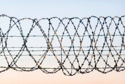 W rapped barbed wire fence with spikes and sky in the background. Rusted chain link fence guarding high security facility like airport, jail or country boarder