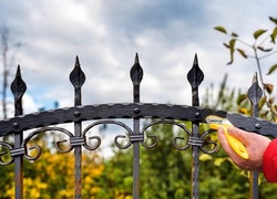 hand with brush painting wrought iron fence 