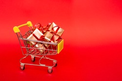 Grocery basket with golden gift boxes with red ribbon on red background banner with copy space. Christmas shopping online. Winter holiday sales, seasonal sales, Black Friday, Christmas, discounts and