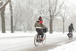 A woman biking in the Amsterdam Vondelpark on a snowy winter day in december in the Netherlands.