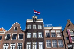 Dutch flag on the canal houses with a blue sky in the center of Amsterdam in the Netherlands.