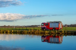 A red firetruck driving on the Lisserdijk along the river the Ringvaart in the village of Lisse in the Province of North-Holland in the Netherlands
