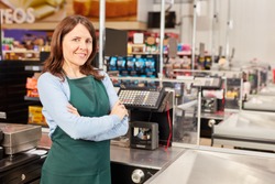 Woman in green apron as a cashier at the cash register in the supermarket or discounter