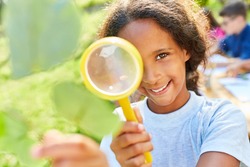 Happy girl in summer school at summer camp looks through magnifying glass at a sheet