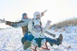 Family with parents and daughter playing toboggan in winter with enthusiasm