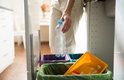 Man putting empty plastic bottle in recycling bin in the kitchen. Person in the house kitchen separating waste. Different trash can with colorful garbage bags. 