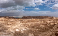 Panoramic landscape of the remote part of the Judean Desert, Israel. Sandstone hills, natural terraces with escarpments and dry wadies of the Judean Desert. Dead sea on the background.