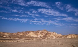 Panoramic view of a wide valley in a remote region of the Negev Desert. Desert beauty in a sunny winter day. Desert landscape with golden mountains and white clouds on the blue sky. Vacation in Israel